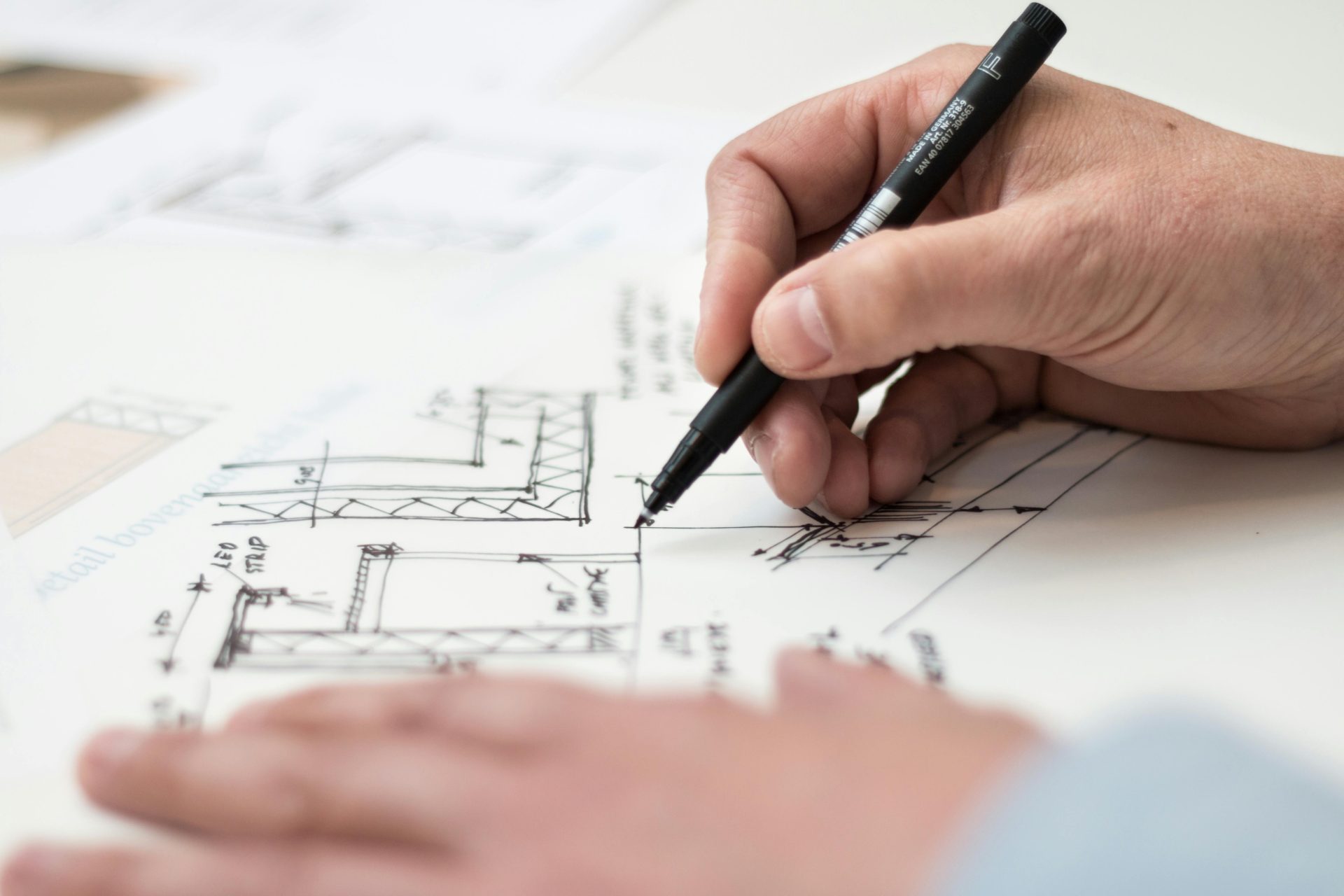 Nahaufnahme einer Handzeichnung komplizierter technischer Designs auf einem Bauplan mit einem Stift, ideal für Themen aus den Bereichen Ingenieurwesen oder Architektur.